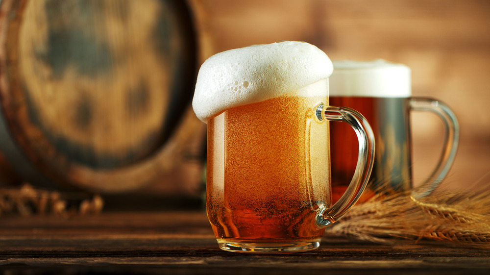 Two glass mugs of beer next to a barrel.