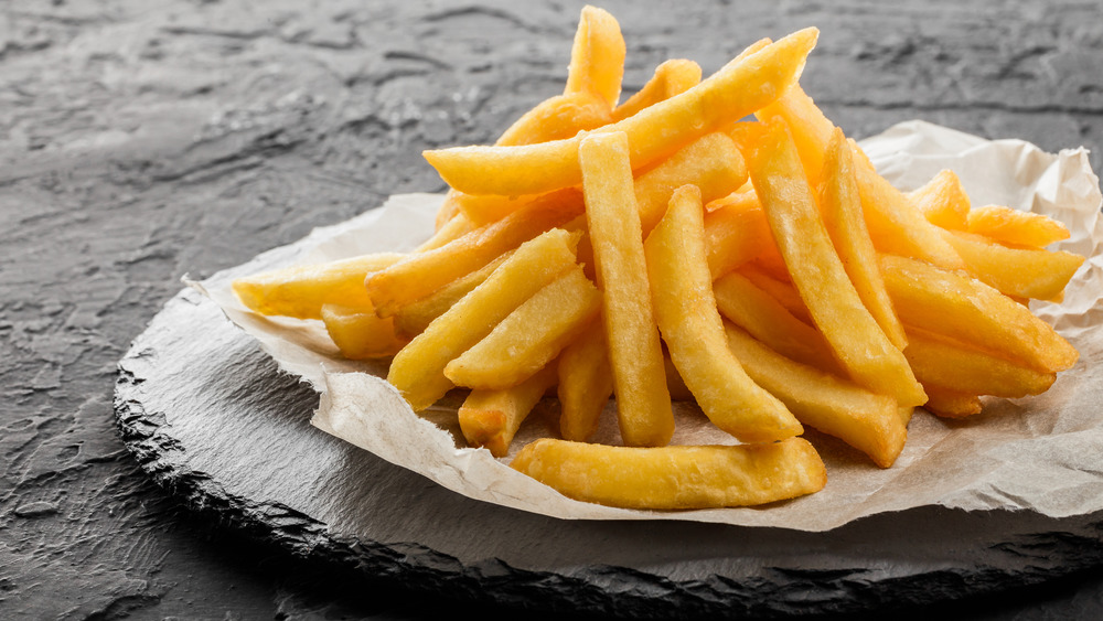 A pile of French fries on a piece of paper on a dark gray stone