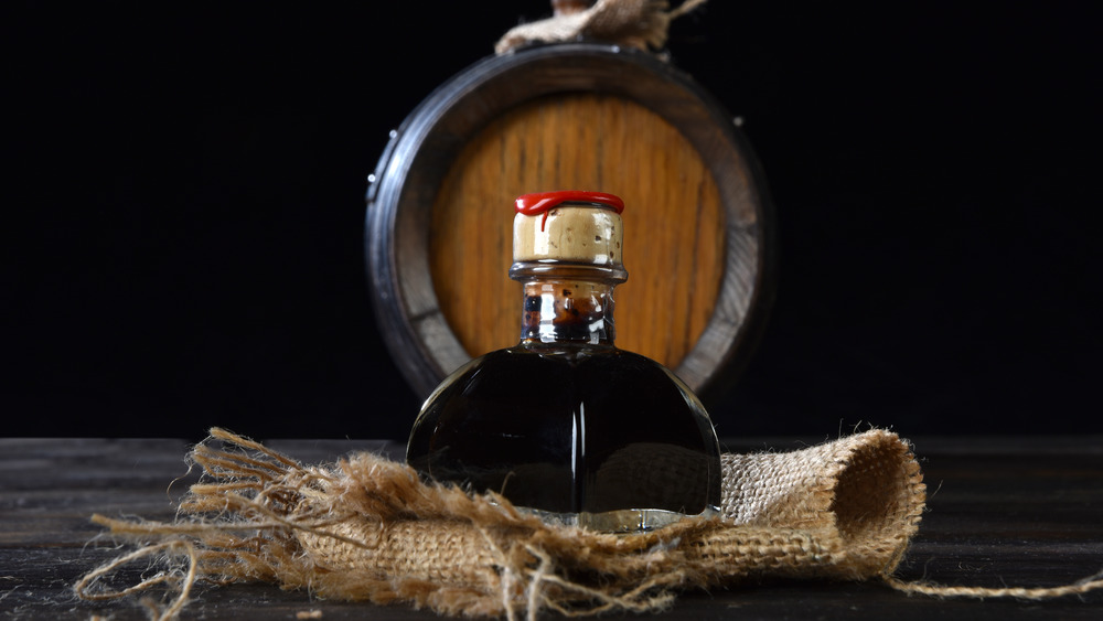 A bottle of balsamic vinegar on burlap in front of a barrel.