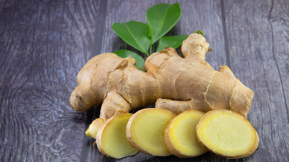 A whole piece of ginger next to sliced pieces of ginger.