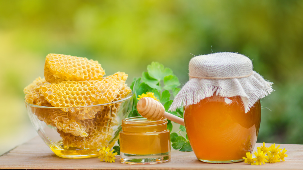 A glass bowl of honey combs next to two containers of honey and yellow flowers.