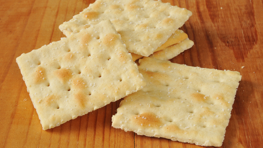 Five saltine crackers piled on a piece of wood.