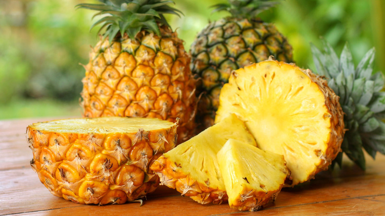 Whole and cut pineapples on a wooden surface