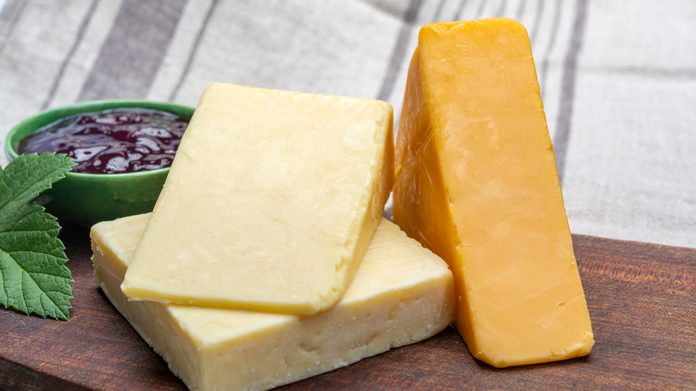 Two types of cheddar cheese on a wooden cutting board