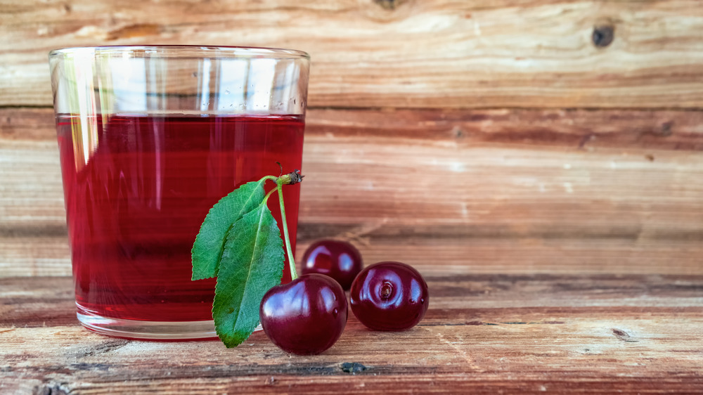 Glass of cherry juice next to three cherries