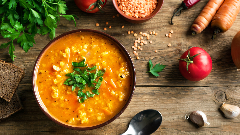 Bowl of lentil dal on a wood background with parsley, tomato, and uncooked lentils