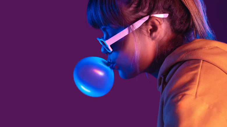 girl blowing gum bubble purple background