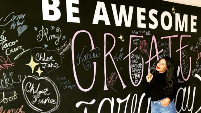 Naz stands in front of a wall that says "Be awesome, create a great day"