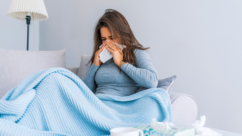 Woman on sofa blowing her nose with flu