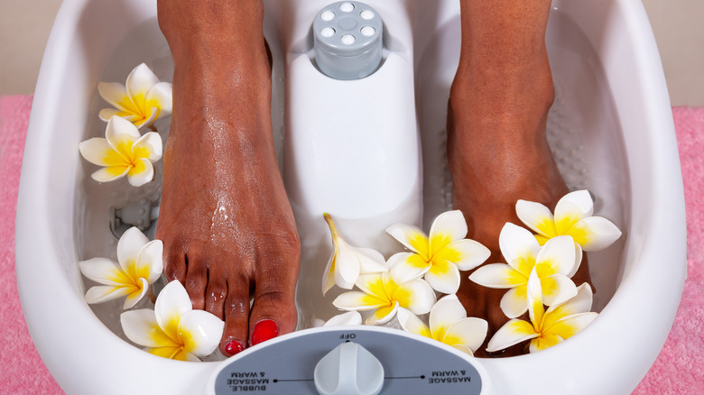 Woman soaking feet in foot bath with flower petals