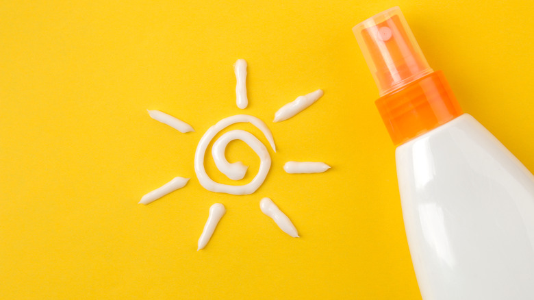 Sunscreen bottle next to a sun drawn with sunscreen lotion on a yellow background