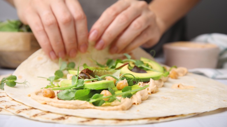 woman's hands making a healthy veggie wrap