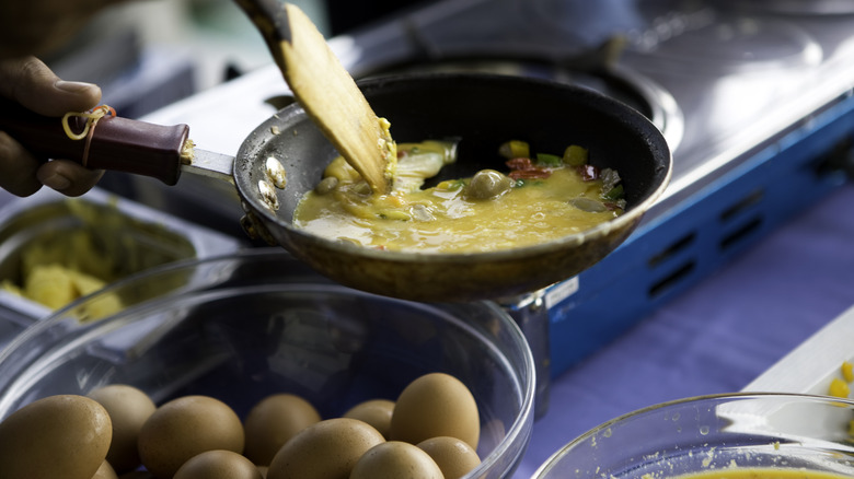 basket of whole eggs with a pan cooking an omelet 