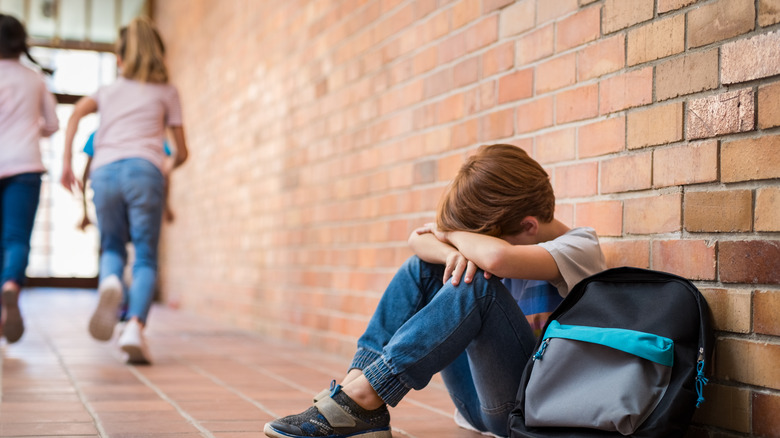 little boy sitting on floor after being bullied by other children