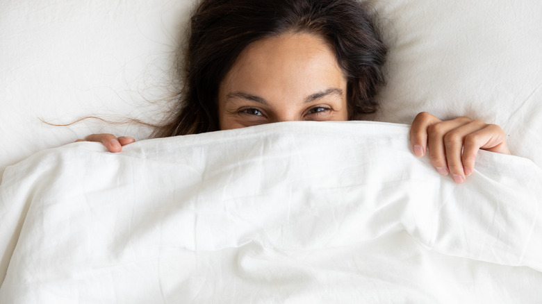 Woman in bed, smiling, hiding half her face