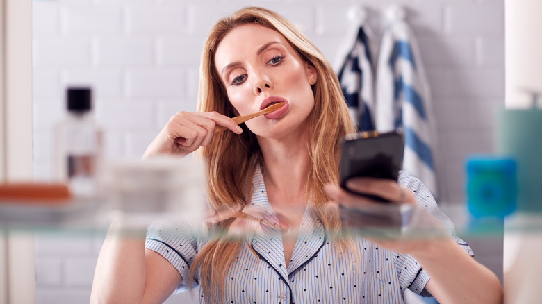 woman using phone while brushing teeth