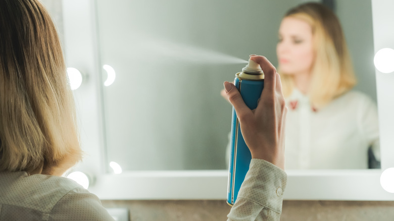 Woman spraying can of hair spray in her hair looking at her reflection in the mirror