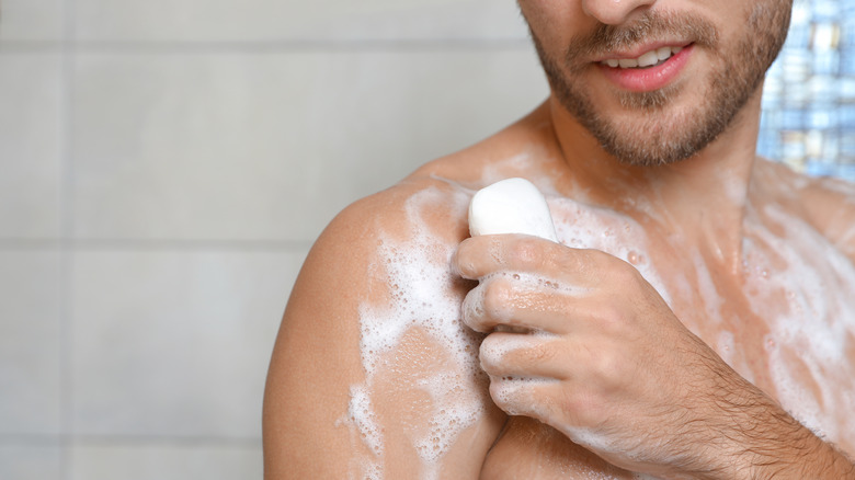 soapy shirtless man in shower with bar of soap