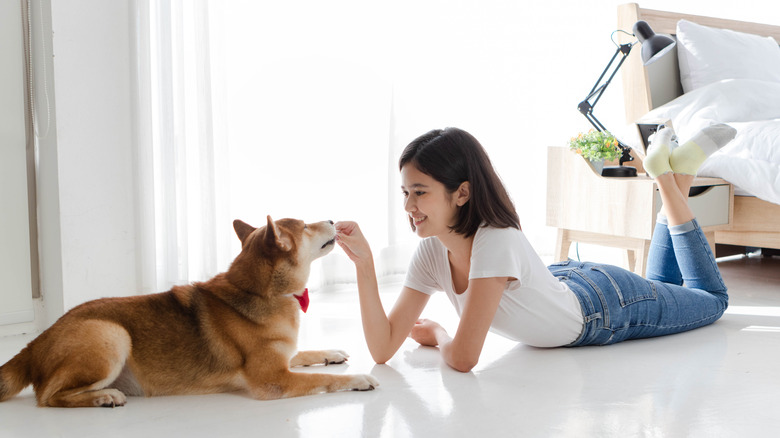 smiling woman laying on floor and hand-feeding her dog