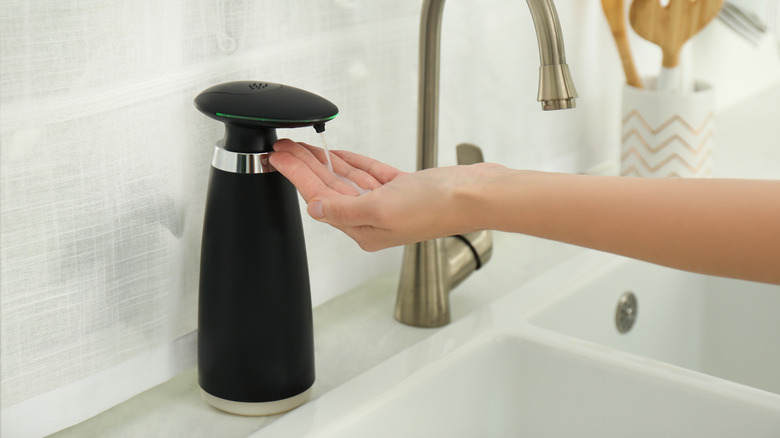 outstretched hand under soap dispenser at sink