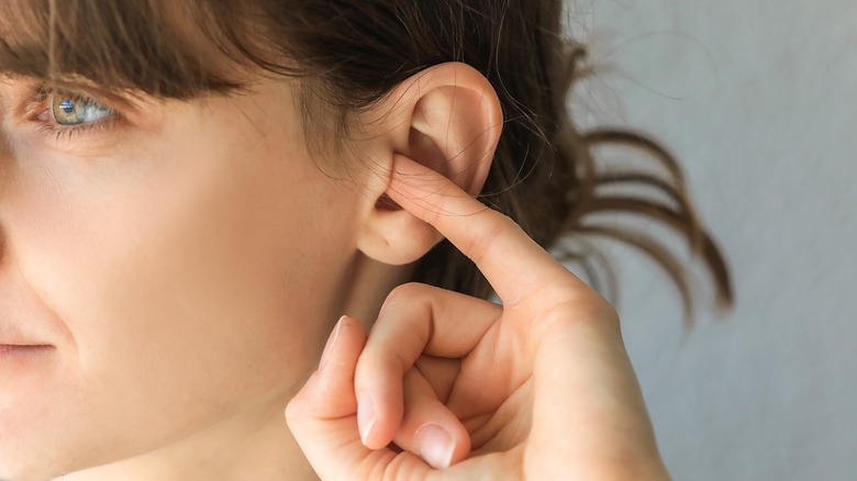 person itching ear with finger