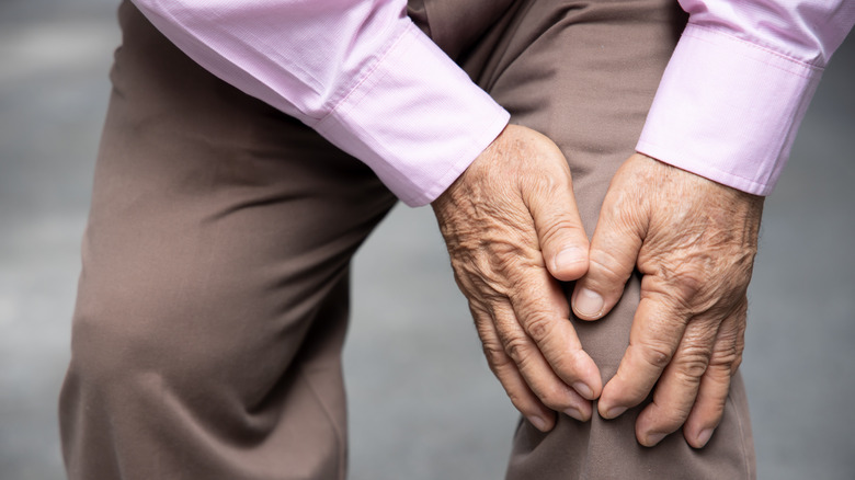 elderly man clutching at knee with both hands