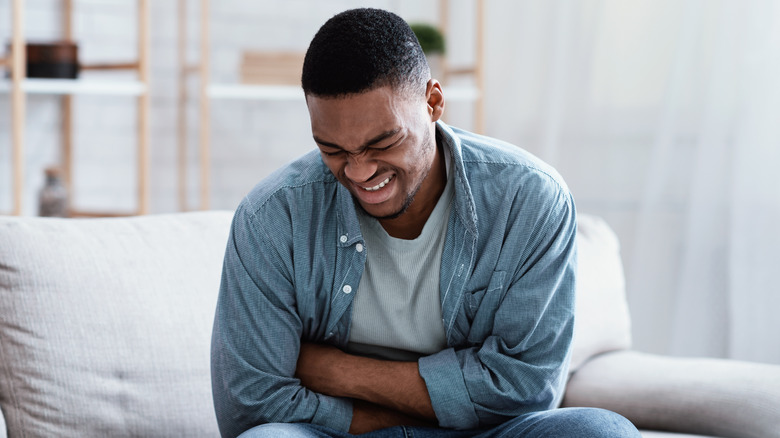 man sitting on a couch and grimacing while holding his stomach