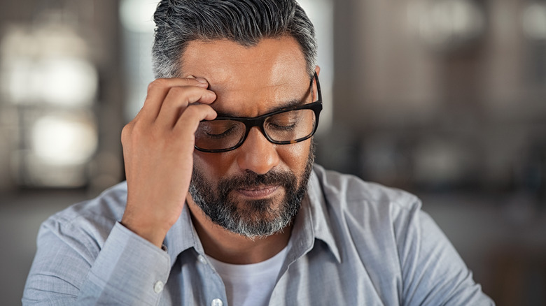 man with a beard and glasses holding the side of his head like he's tired