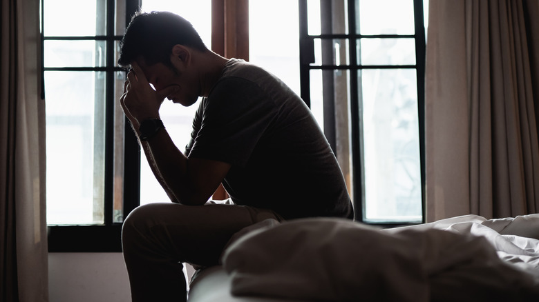 man in shadow sitting and holding his head next to windows