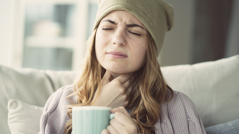 Woman holding tea and touching throat