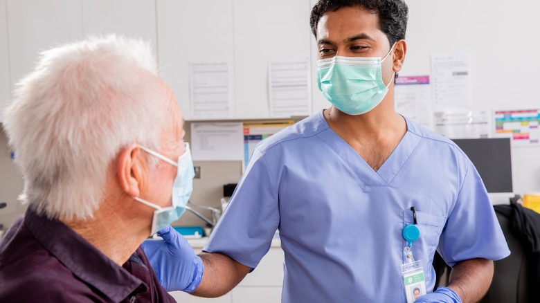 Doctor wearing a face mask touching the shoulder of an older patient wearing a face mask