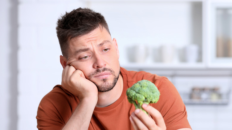 man staring unhappily at broccoli disgusted