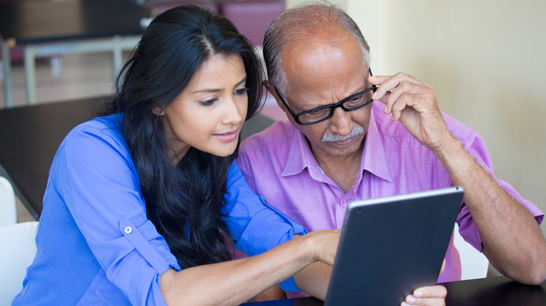 daughter assisting elderly father on tablet