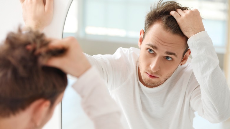 young man looking worried about hair in mirror