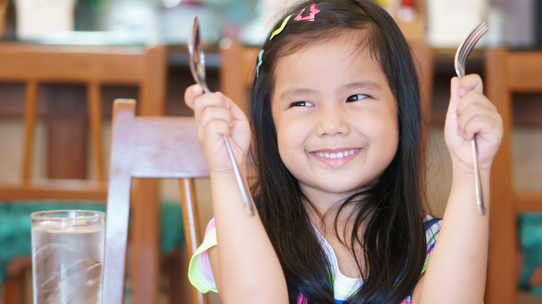 child smiling with knife and spoon