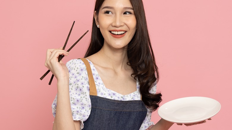 smiling woman holding plate and chopsticks