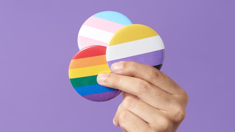 Hand holding rainbow, trans, and non-binary flag pins
