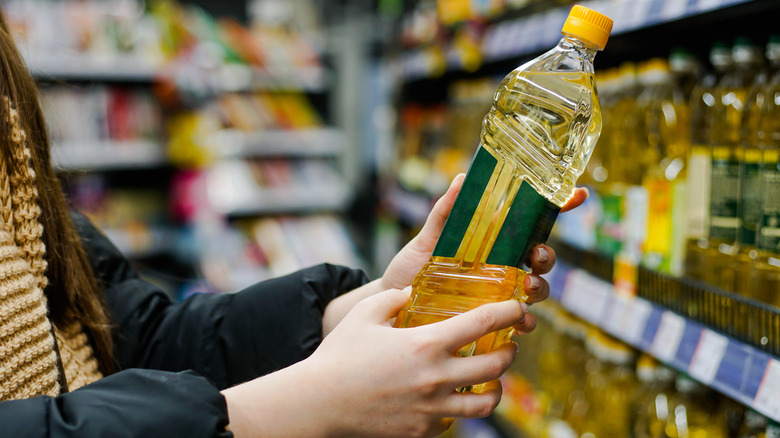 Woman holding vegetable oil in supermarket aisle