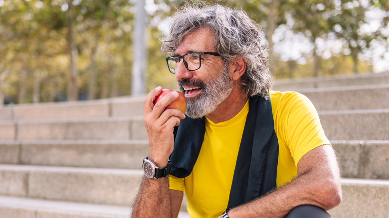 An older man eating an apple while sitting on a step