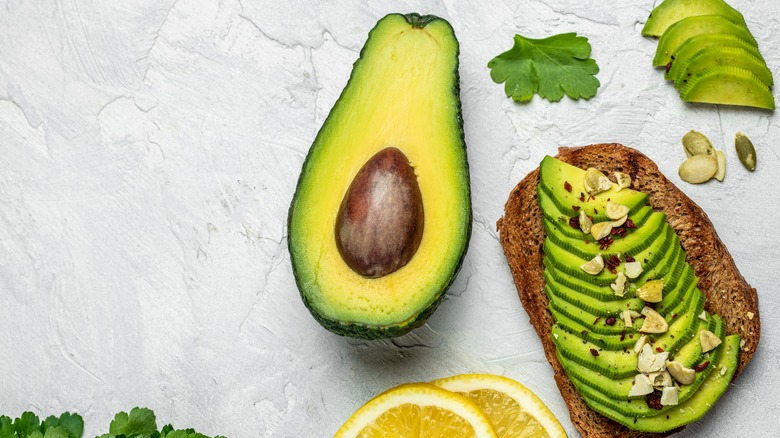 half an avocado and avocado spread over toast with slices