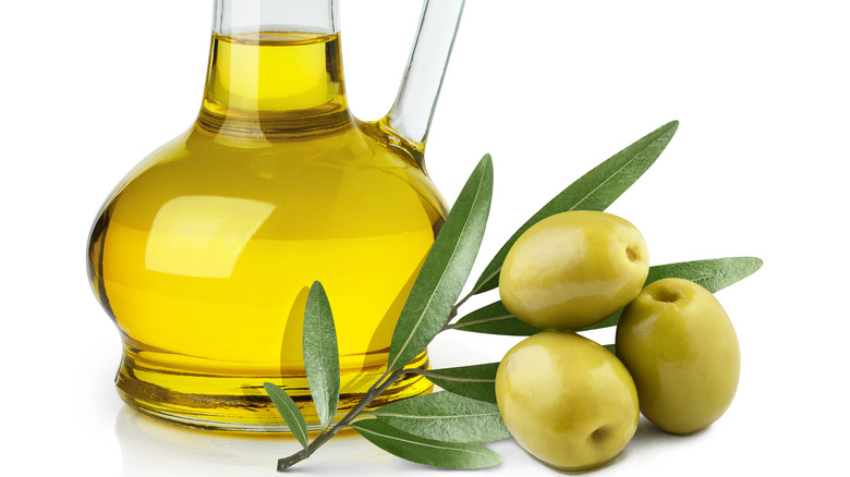 olive oil bottle next to olives and olive leaves