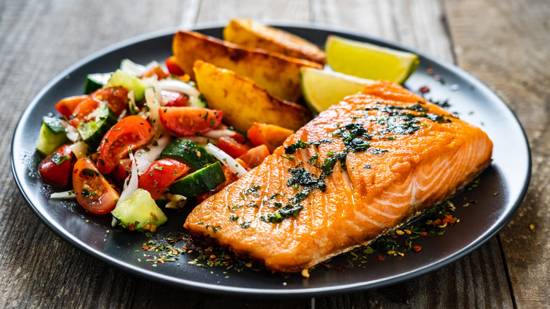 a plate of salmon with salad and potatoes