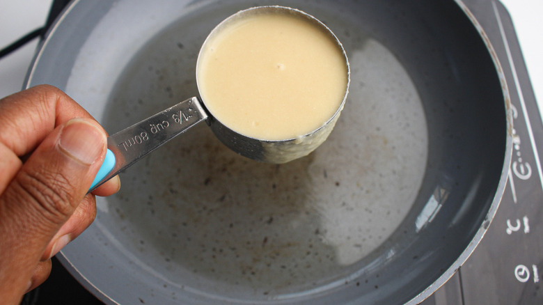 measuring spoon with batter over frying pan