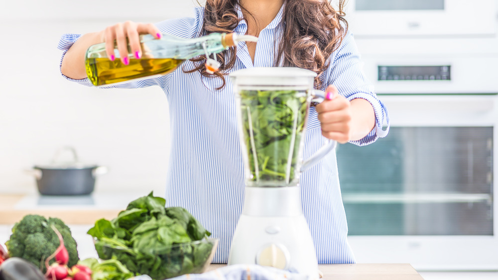 woman adding olive oil to smoothie
