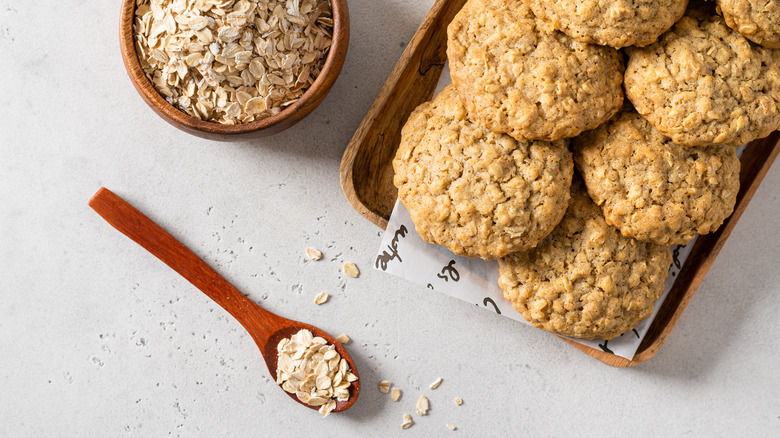 homemade oatmeal cookies next to a spoon and bowl containing oats