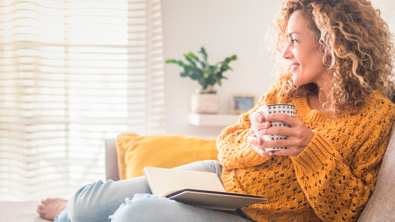 Woman relaxing at home with cup of tea and book