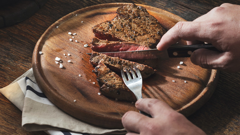 man's hand cutting steak on plate