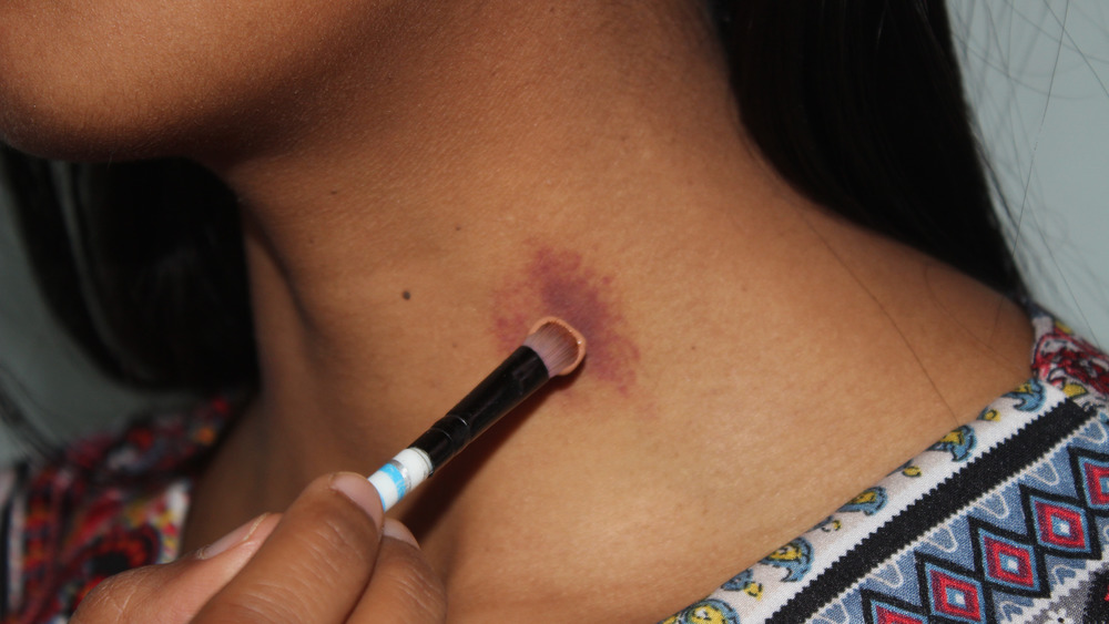 Close up of woman applying make up to cover up hickey on neck