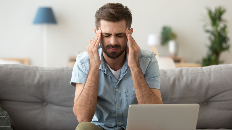 Man sitting at computer clasping his head in pain