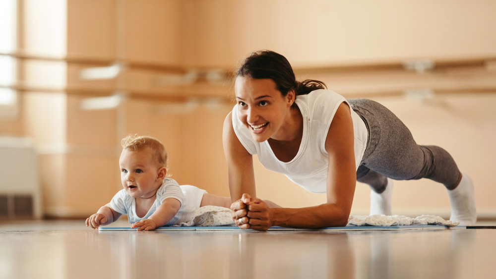 Athletic mother exercising in plank position while being with her baby